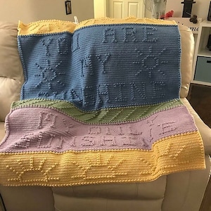 Puede incluir: Una manta de crochet multicolor con las palabras "You are my sunshine" en letras en relieve. La manta está hecha con una variedad de colores, incluyendo amarillo, verde, morado y azul.