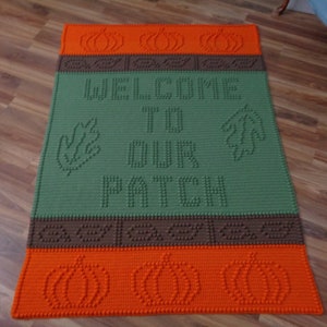 Puede incluir: Una alfombra de bienvenida de crochet verde con el texto "Welcome to our patch" y diseños de calabazas naranjas.