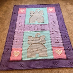 Puede incluir: Una manta de ganchillo en tonos morado, rosa y turquesa. La manta presenta dos diseños de elefantes y las palabras "LOVE YOU TO INFINITY" en disposición vertical. Hay corazones en las esquinas. La manta es rectangular.