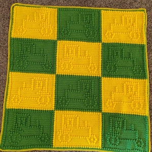 May include: A crocheted baby blanket with a checkerboard pattern in yellow and green. The blanket features a repeating design of a small truck.