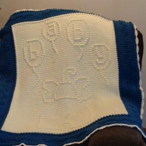 May include: A crocheted baby blanket with a white center and a blue border. The center of the blanket features a repeating pattern of small circles.