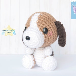 Pode incluir: Um brinquedo de cachorro beagle de croch&ecirc; com orelhas marrons, p&ecirc;lo branco e manchas marrons. O brinquedo est&aacute; sentado em uma superf&iacute;cie branca.