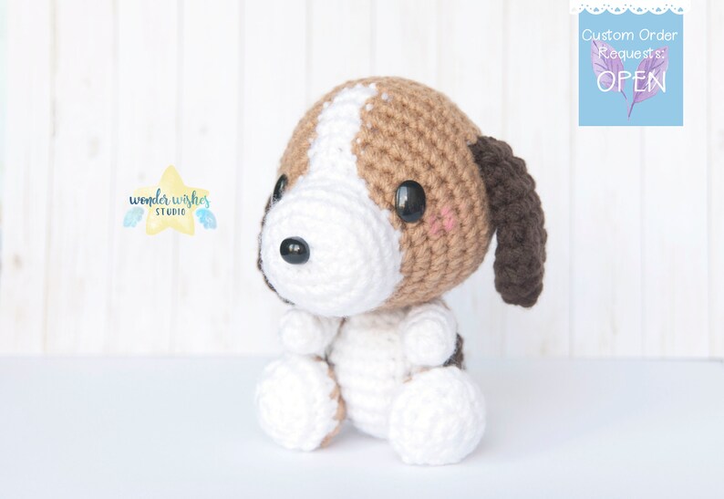 Pode incluir: Um brinquedo de cachorro beagle de croch&ecirc; com orelhas marrons, p&ecirc;lo branco e manchas marrons. O brinquedo est&aacute; sentado em uma superf&iacute;cie branca.