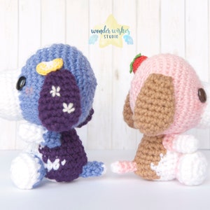 Pode incluir: Dois c&atilde;es de pel&uacute;cia de croch&ecirc;, um azul e roxo com uma flor amarela na cabe&ccedil;a, e o outro rosa e marrom com um morango na cabe&ccedil;a.