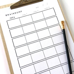 May include: A white clipboard with a wooden frame and a silver clip. The clipboard has a grid of boxes labeled "note 1", "note 2", "note 3", and "date". The clipboard is on a white surface with a black pencil.
