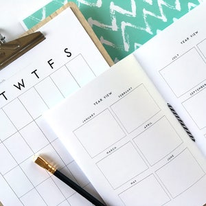 May include: A white planner with a monthly calendar and a yearly calendar view. The monthly calendar has the days of the week labeled "SMTWTFS". The yearly calendar has each month labeled with its name. The planner is open to the yearly calendar view.