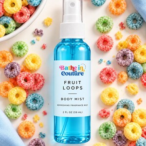 May include: A clear plastic spray bottle filled with blue liquid, featuring a white label that reads Bathe in Couture FRUIT LOOPS BODY MIST 2 FL OZ (59 mL), surrounded by scattered colorful ring-shaped cereal pieces on a white surface.