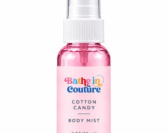 May include: A clear pink plastic spray bottle of body mist with a white cap. The label reads Bathe in Couture, Cotton Candy, Body Mist, and 2 oz (59 mL). The bottle has a white pump mechanism and a clear plastic overcap.
