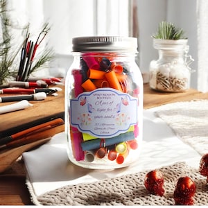 May include: A glass jar filled with colorful rolled up paper slips. The jar has a silver lid and a white label that reads "SPIRIT BLOSSOM BOUTIQUE A jar of light for your soul's 55 Affirmation Quotes for Peace & Love".