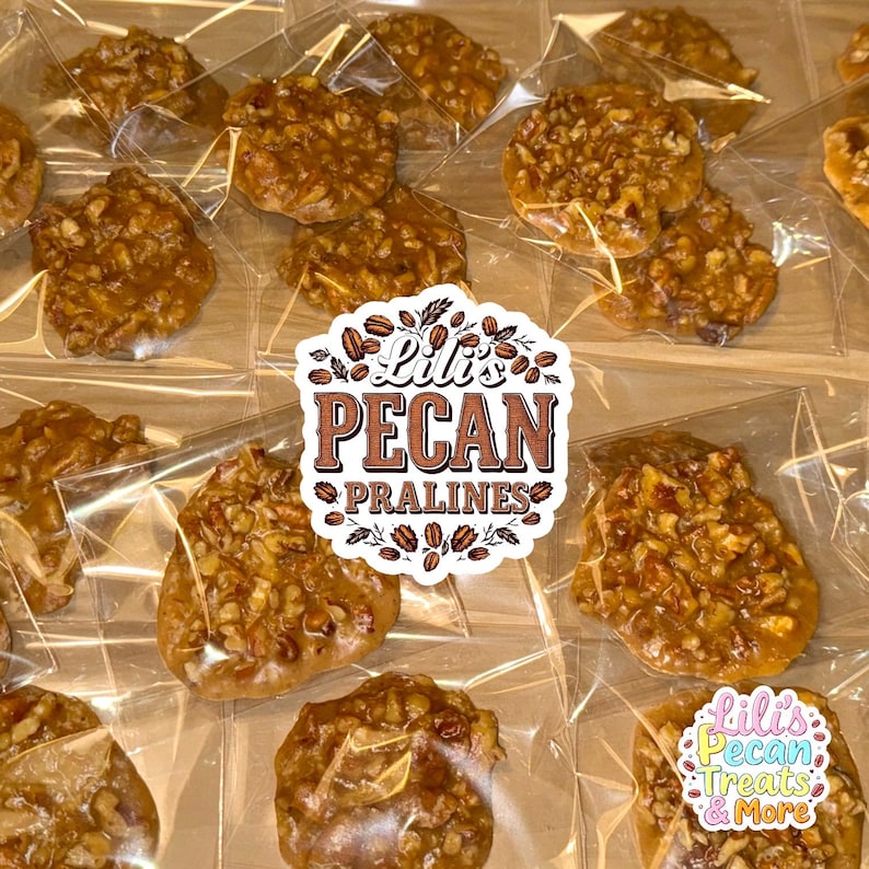 May include: Multiple individual pecan pralines packaged in clear plastic wrappers. A central white sticker features the text Lili's PECAN PRALINES surrounded by pecan illustrations. A smaller sticker reads Lili's Pecan Treats & More.