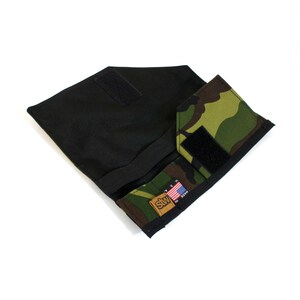 Op de afbeelding: Een zwarte en camouflage stoffen portemonnee met een klittenbandsluiting en een klein Amerikaans vlagpatch met de tekst "Made in USA".