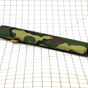 Puede incluir: Un tubo de tela con estampado de camuflaje, una costura negra y una etiqueta de cuero marr&oacute;n.