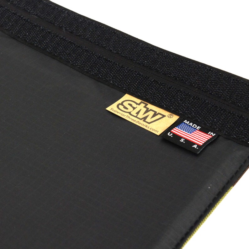 Puede incluir: Primer plano de una tela negra con una etiqueta dorada que dice "stw SuperiorThreadworks.com" y una peque&ntilde;a bandera estadounidense con el texto "Made in U.S.A."