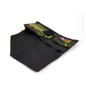 Op de afbeelding: Een zwarte en groene camouflage stoffen tas met een klittenbandsluiting en een klein Amerikaans vlagpatch. De tas is open en de binnenkant is zwart.