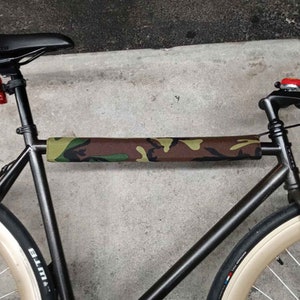 Puede incluir: Una bicicleta negra con un protector de cuadro de camuflaje. La bicicleta tiene un sill&iacute;n negro, un manillar negro y neum&aacute;ticos de color beige.