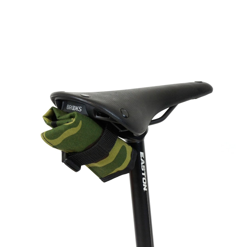 Op de afbeelding: Een zwart Brooks-zadel met een groene en bruine camouflage zadeltas die aan de onderkant is bevestigd. Het zadel is gemonteerd op een zwarte Easton zadelpen.
