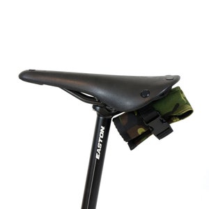 Op de afbeelding: Een zwart zadel voor een fiets met een camouflage tas die aan de onderkant is bevestigd. De zadelpen is zwart en heeft het woord "EASTON" in wit erop gedrukt.