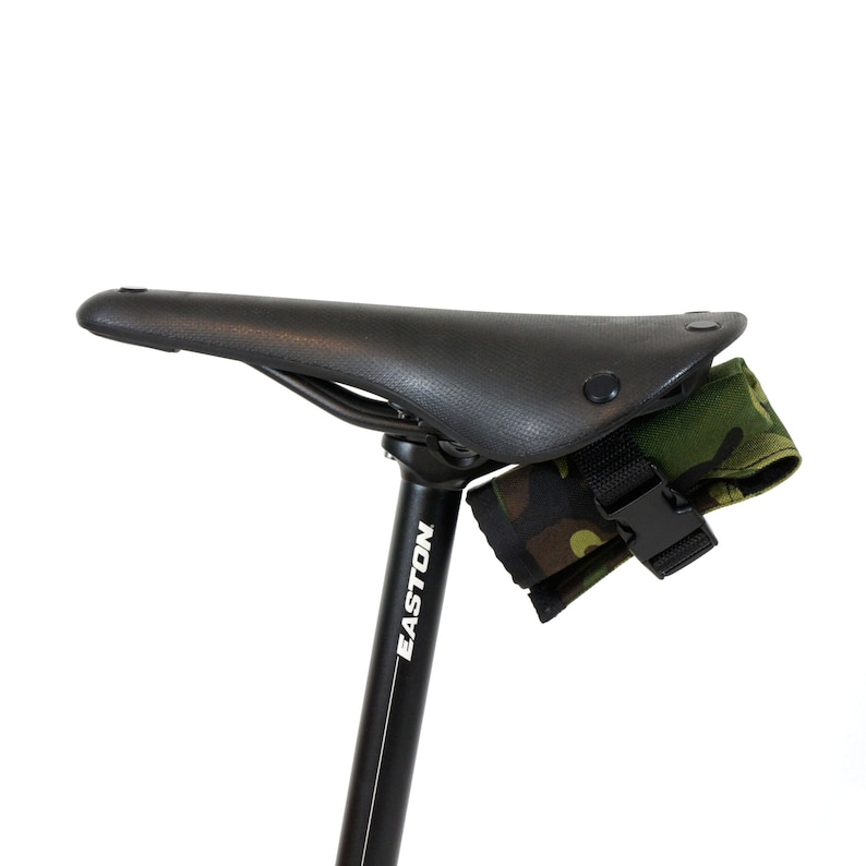 Op de afbeelding: Een zwart zadel voor een fiets met een camouflage tas die aan de onderkant is bevestigd. De zadelpen is zwart en heeft het woord "EASTON" in wit erop gedrukt.