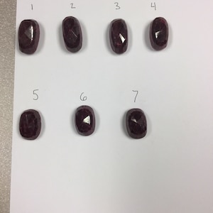 May include: Seven red gemstones, labeled 1 through 7, are arranged in two rows on a white surface. The gemstones are oval-shaped and have a faceted cut.