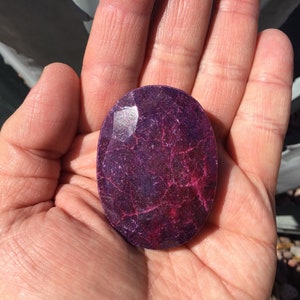 May include: A large, oval-shaped, purple gemstone with a textured surface. The gemstone has a deep purple color with hints of pink and white.