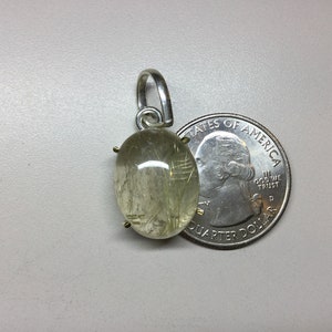 May include: A silver pendant with a clear, oval-shaped gemstone with gold flecks. The gemstone is about the size of a US quarter.
