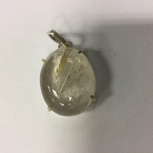 May include: A silver pendant with a clear quartz stone featuring gold inclusions. The stone is oval shaped and set in a silver bezel.