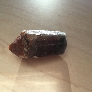 May include: A dark purple and brown crystal with a pointed end. The crystal has a rough, natural texture.