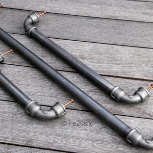 Peut inclure: Trois poignées de tuyau en métal noir avec des accents en cuivre. Les poignées sont alignées sur une surface en bois.