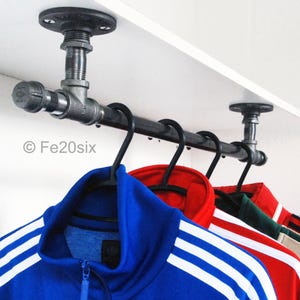 May include: A black metal pipe shelf with a white shelf and a black metal pipe rod for hanging clothes. The rod has five black hangers with clothes hanging on them. The clothes are blue, red, green, white, and black.