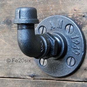 May include: Black metal pipe hook with a flange and a 90-degree bend. The flange has the text "1949" on it.