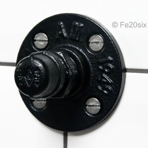 May include: Black metal pipe flange with a round cap and four screws. The flange has the text "1/2" and "A.M." on it.