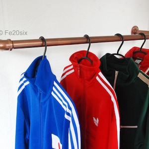 May include: A copper pipe clothing rack with five jackets hanging on it. The jackets are blue, red, green, beige, and black. The rack is mounted to a white wall. ©Fe20six