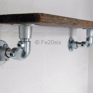 May include: A rustic wooden shelf with two silver metal pipe brackets. The shelf is mounted to a white wall.