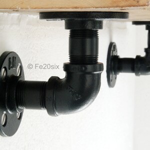May include: Black industrial pipe shelf brackets. The brackets are made of black metal and feature a flange design for wall mounting. The design includes 90-degree elbows and threaded pipe sections. The brackets are shown mounted on a wooden shelf.