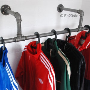 May include: A metal pipe rack with five black hangers holding various jackets. The jackets are red, green, black, and blue. The rack is mounted to a white wall. ©Fe20six