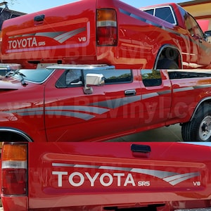Könnte beinhalten: Roter Toyota SR5 V6 Pickup-Truck mit grauen und silbernen Akzentstreifen. Der Truck hat eine verchromte Stoßstange und Seitenspiegel. Das Toyota-Logo sowie die SR5- und V6-Bezeichnungen sind am Heck sichtbar.