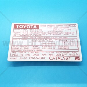 May include: A red and white sticker with the text "TOYOTA VEHICLE EMISSION CONTROL INFORMATION" and "CATALYST VA". The sticker contains information about the engine family, engine size, and ignition timing specifications for a 1992 Toyota 5S-FE engine.