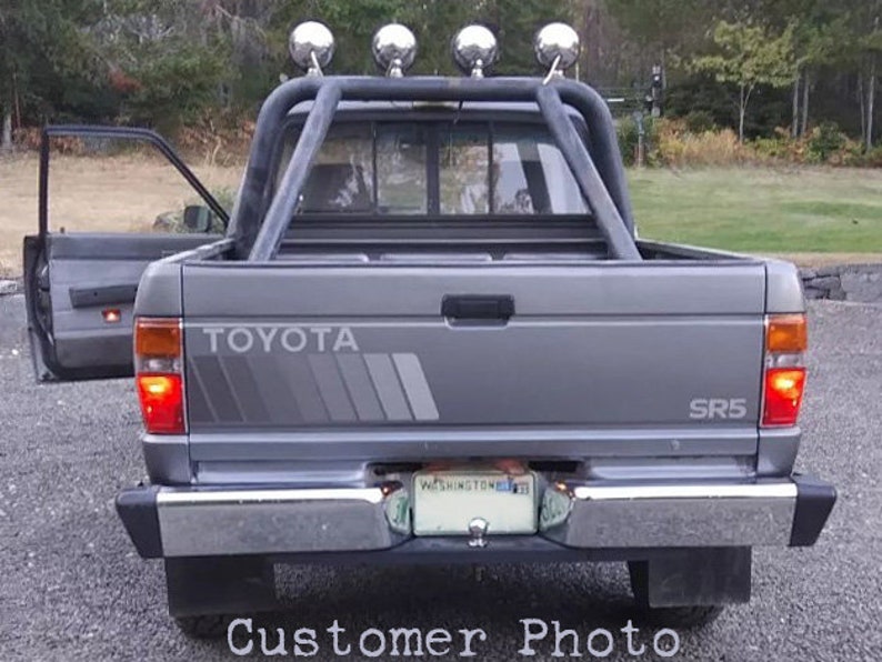 K&ouml;nnte beinhalten: Ein grauer Toyota SR5 Pickup-Truck mit &Uuml;berrollb&uuml;gel und vier Scheinwerfern. Der Truck hat eine Chromsto&szlig;stange und ein Nummernschild aus Washington. Der Text "Customer Photo" befindet sich am unteren Rand des Bildes.