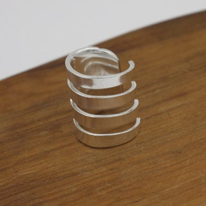 May include: Silver ring with four stacked bands. The bands are open on one side and are smooth and shiny.