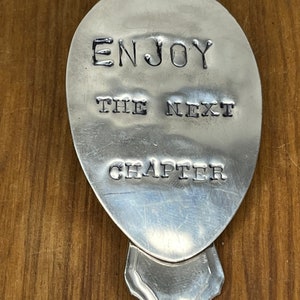 Pode incluir: Uma colher de prata com as palavras "Enjoy the next chapter" gravadas.