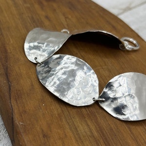 The beautiful textured spoon bowl bracelet resting on a dark brown board that shows off it's texture and shine.
