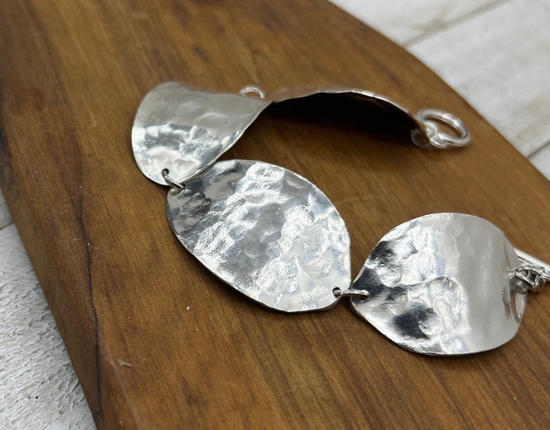 The beautiful textured spoon bowl bracelet resting on a dark brown board that shows off it's texture and shine.