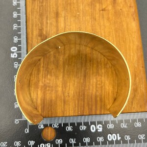 May include: A gold-coloured metal cuff bracelet, shown from the inside, on a wooden surface.