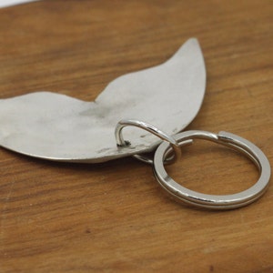 May include: Silver whale tail keychain with a silver ring. The whale tail is a simple design with a smooth surface.