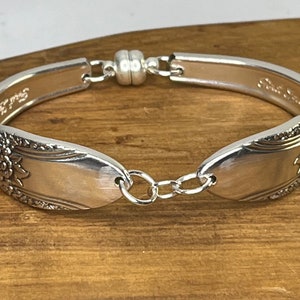 Op de afbeelding: Zilveren lepels armband met een magnetische sluiting en een ketting detail. De lepel heeft een bloemmotief.
