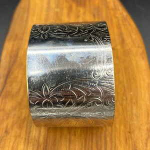 May include: Silver napkin ring with an ornate floral design.