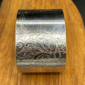 May include: Silver cuff bracelet with an intricate floral design.
