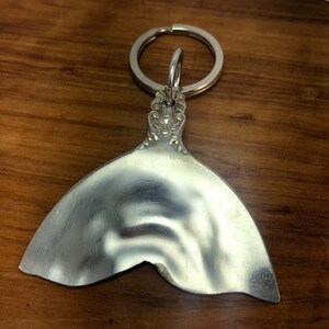 May include: Silver mermaid tail keychain with a decorative top and a ring for attaching keys.