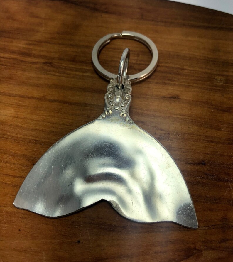 May include: Silver mermaid tail keychain with a decorative top and a ring for attaching keys.