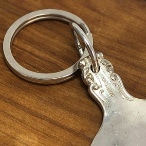 May include: Silver spoon keychain with a decorative handle and a ring attached. The spoon has the word "Pat. No." engraved on the back.